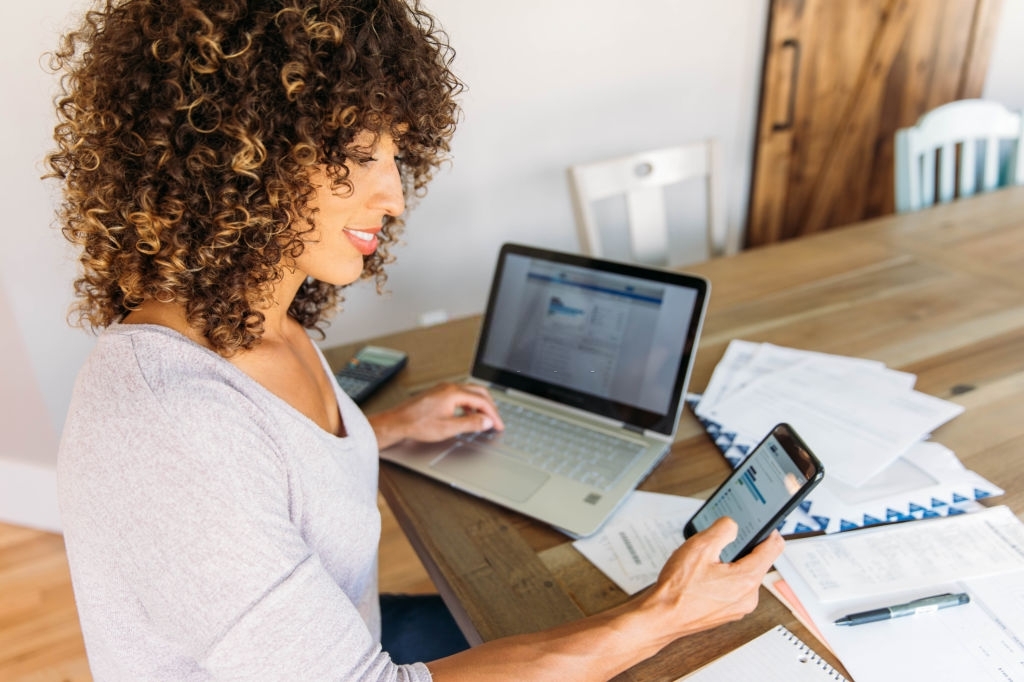 A woman sits with her laptop and financial reports doing her monthly budget. 